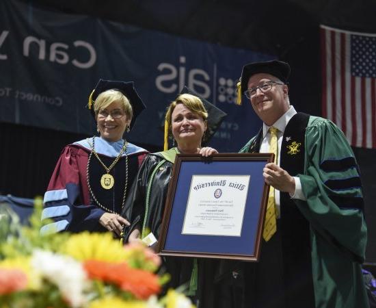 职业治疗教授Mary Siniscaro站在教务长Todd Pfannestiel和校长Laura casmento之间, 在2023年本科毕业典礼上颁奖.