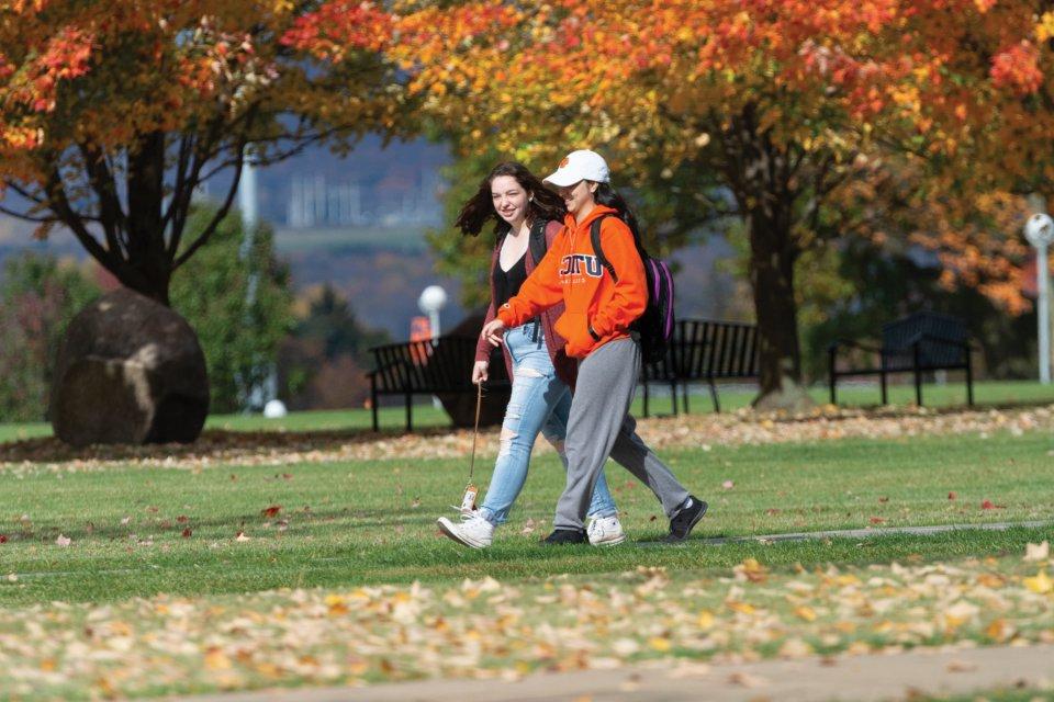 两个学生穿过校园，在秋天的红色、橙色和黄色的树中穿行.